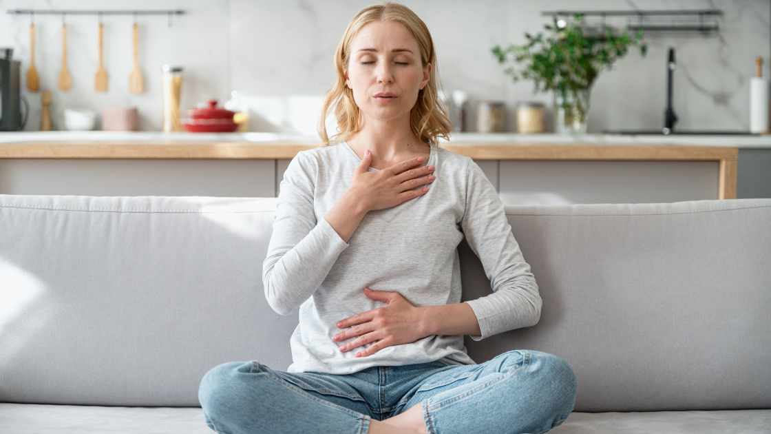 Woman practicing mindful breathing at home with hands on chest and abdomen, symbolizing Nirvana Recovery’s use of mindfulness techniques to support emotional healing in addiction recovery.