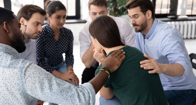 Support group comforting a distressed woman, symbolizing the crucial role of empathy, community, and peer support systems in the recovery journey from addiction.