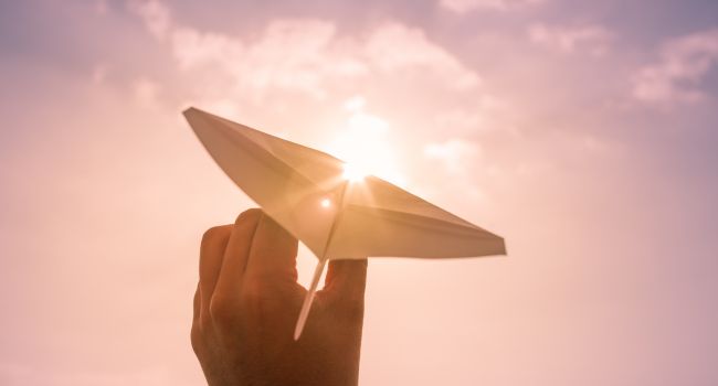 A hand holding a paper airplane against the sunlight, symbolizing new beginnings, goal setting, and direction during the assessment phase of recovery.