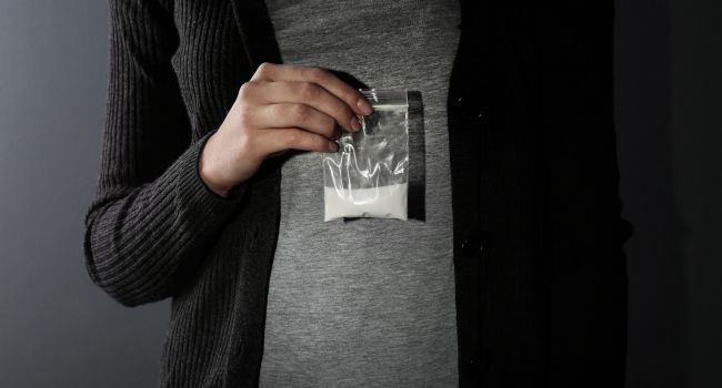 A person holding a small plastic bag of white powder, symbolizing the dangers and reality of drug possession and addiction struggles.
