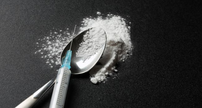 A syringe, spoon, and white powder on a dark surface, symbolizing the dangerous progression of meth use from experimentation to full-blown addiction and its associated health risks.