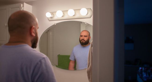 Man looking at himself in the bathroom mirror, reflecting personal growth and self-esteem building in meth recovery.