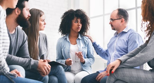 A support group sits in a circle, attentively listening and comforting a distressed woman, illustrating the importance of providing emotional support during withdrawal.