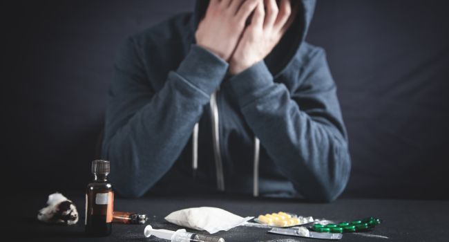 A person in a hoodie sits with head in hands, surrounded by drug paraphernalia, symbolizing emotional distress and continued substance use, signs that meth addiction treatment may not be effective.