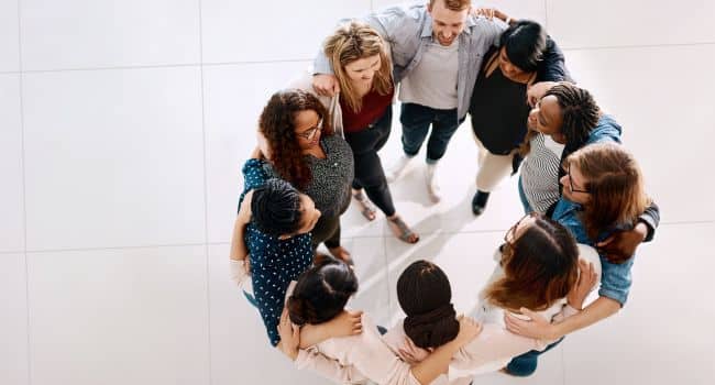 Diverse group of people standing in a supportive circle, arms around each other, symbolizing community, connection, and group therapy as effective strategies for long-term recovery from addiction.