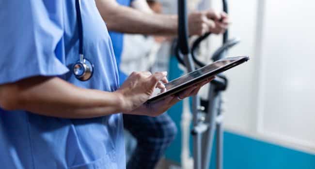 Healthcare professional using a tablet while patients exercise in the background, highlighting options for Arizona alcohol treatment that allow professionals to balance work commitments and recovery.