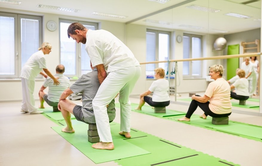 Therapists assist seniors practicing seated yoga on blocks in a group, illustrating continued aftercare and life after rehab.
