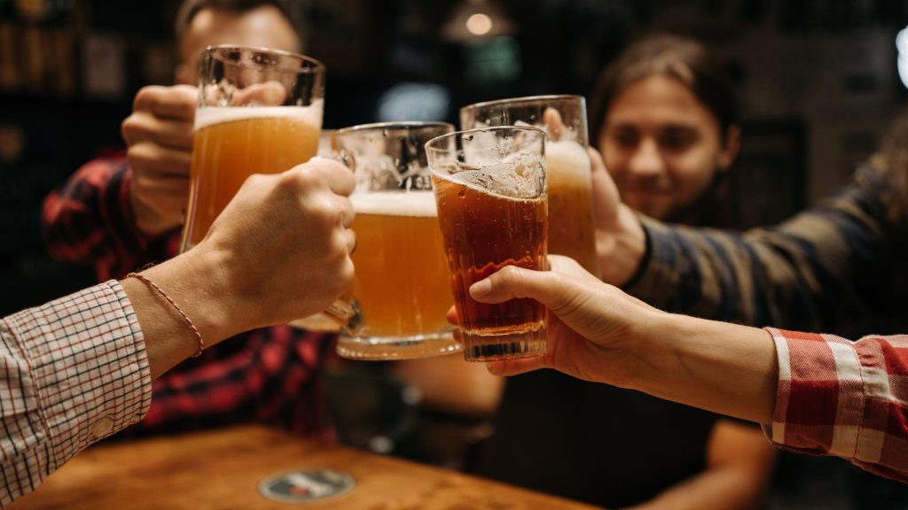 Close-up of young people clinking beer glasses in a bar, representing youth drinking culture and alcohol consumption trends in Arizona.