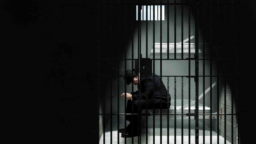 Person sitting in a dimly lit jail cell, representing legal consequences of heroin possession and identification.