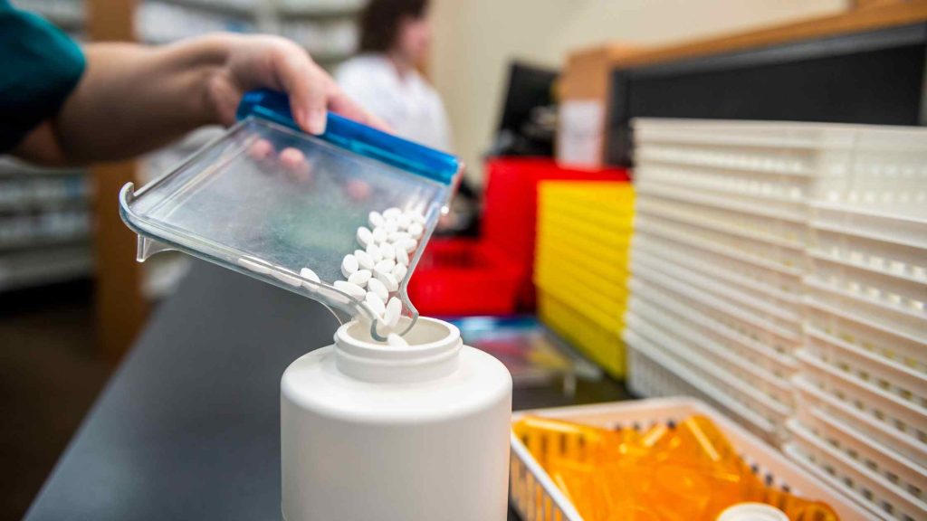 Pharmacist pouring white pills into a container, symbolizing opioid detox services and insurance coverage.